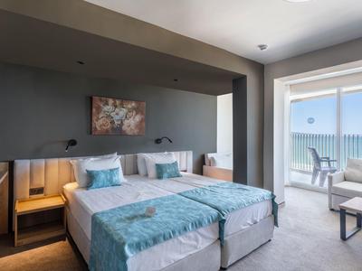 Modern hotel room with two single beds, blue accents, and sea view from the balcony.