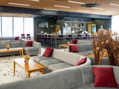 Modern hotel lounge with gray sofas, red cushions, and light wood interior