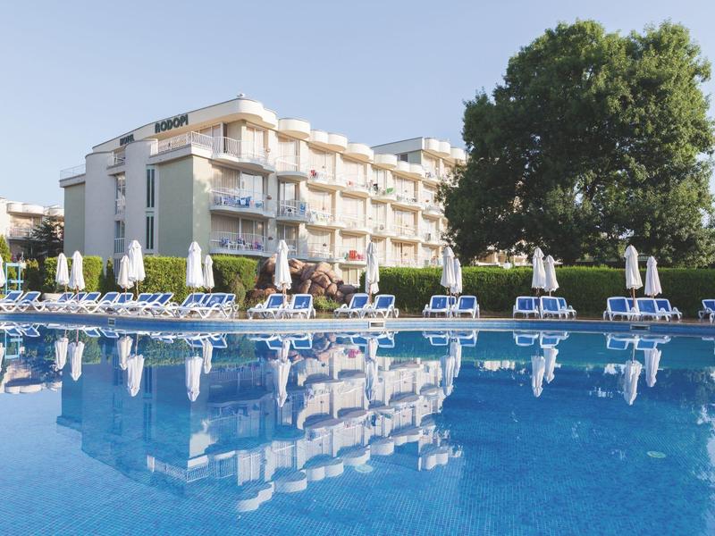 Hotel building with outdoor pool, sun loungers, and umbrellas on a sunny day.