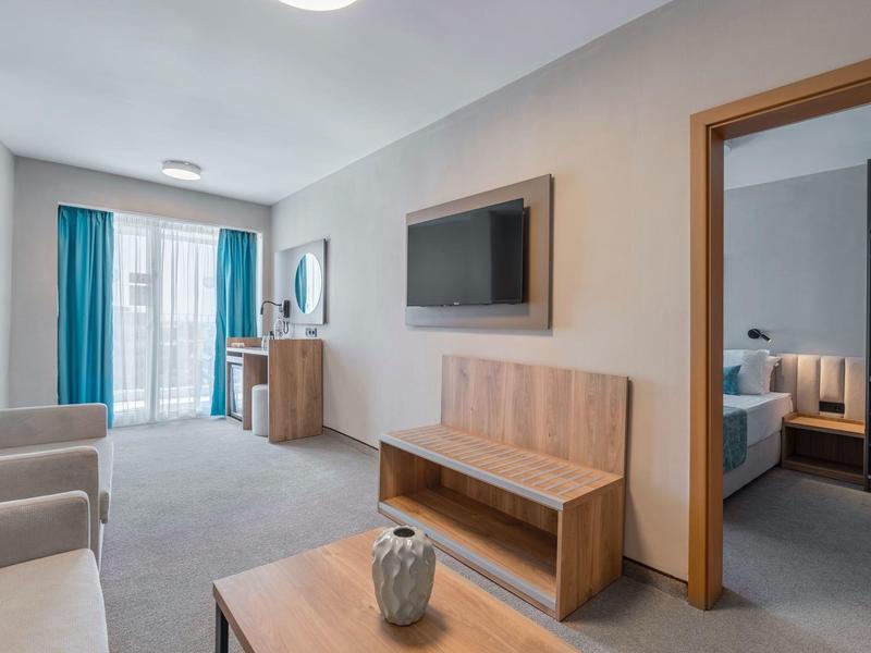 Modern hotel room with living area, TV, desk, and balcony view