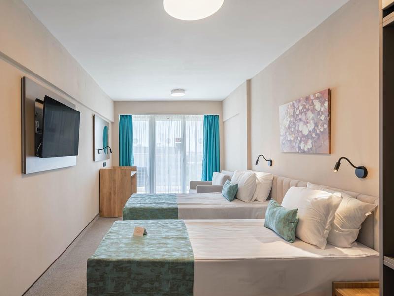 Modern hotel room with two beds, wall-mounted TV, and large window with outside view.