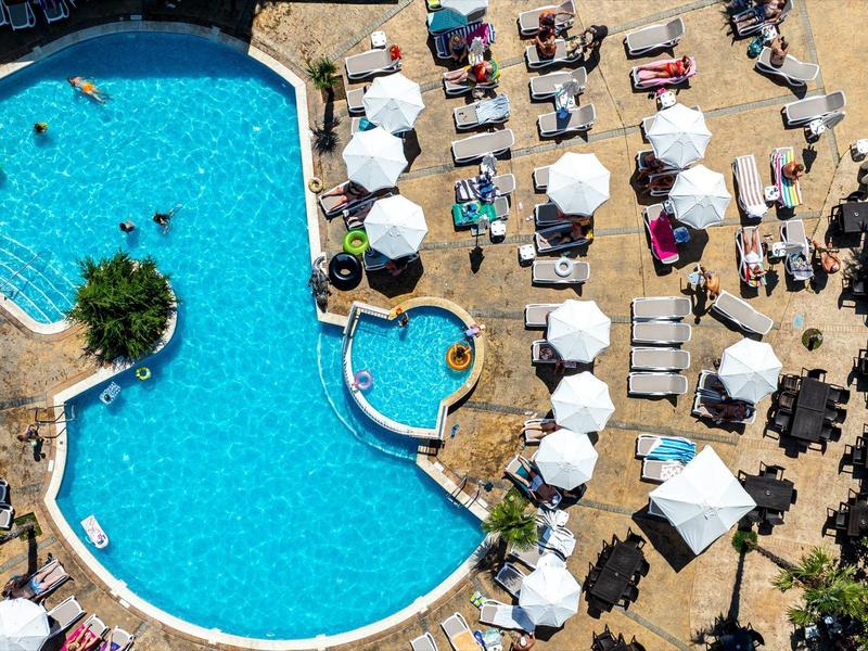 Large hotel pool with loungers, umbrellas, and people around outdoors.