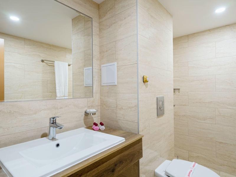 Bright bathroom with white sink, large mirror, and beige tiled walls.