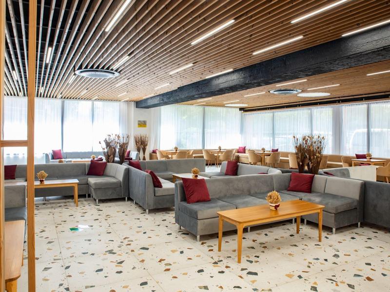 Bright hotel lounge area with gray sofas, wooden tables, and large windows