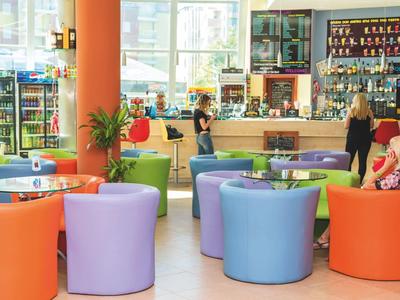 Bunte Sitzgruppen und Theke in hellem, modernem Café mit großen Fenstern und Pflanzen.