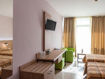 Modern eingerichtetes Hotelzimmer mit zwei Betten, grünem Sessel, Fernseher und Vorhängen am Fenster.