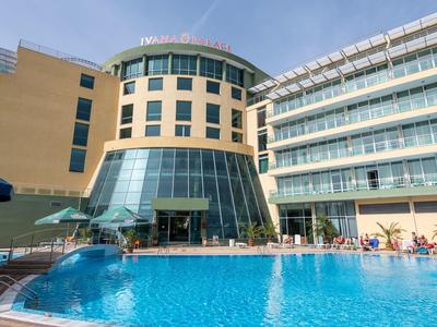 Großer blauer Hotelpool vor modernem, mehrstöckigem Gebäude mit Glas- und Sandsteinfassade.