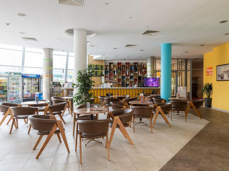 Lichte hotel lounge met houten stoelen, tafels en een grote bar op de achtergrond.