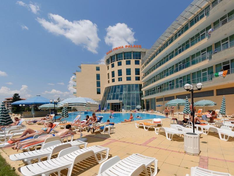 Hotel met buitenzwembad, ligstoelen en gasten op een zonnige dag.