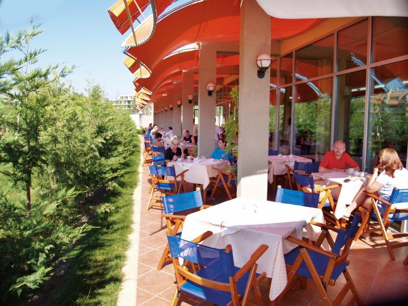 Buitenterras van een restaurant met blauwe stoelen en witte tafelkleden naast groen.