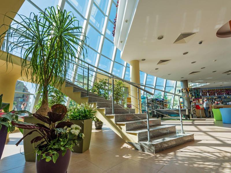 Hel verlichte binnenruimte met planten en trap in een modern hotel.