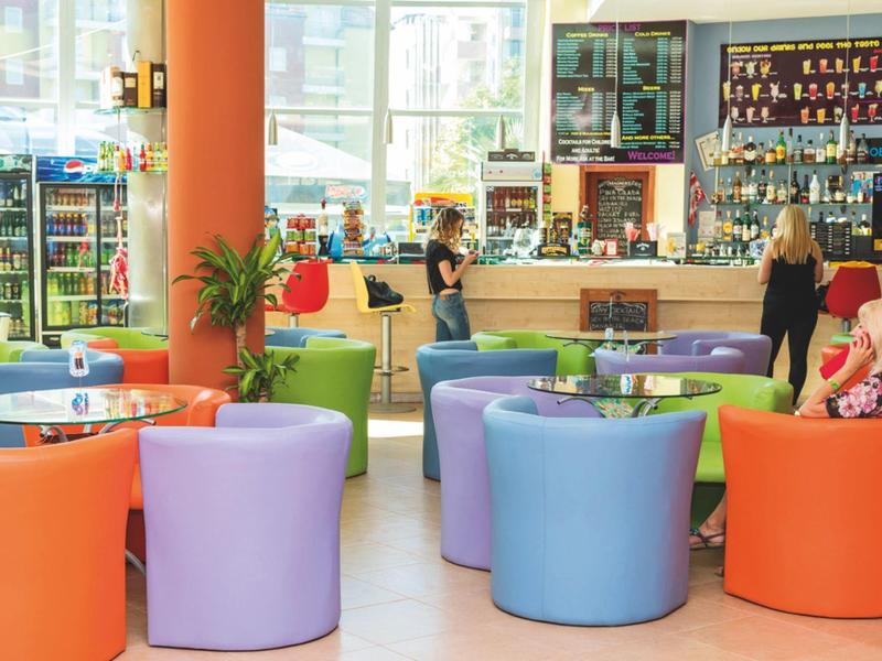 Kleurrijke zitplaatsen in een lichte hotelbar met gasten en personeel aan de bar.