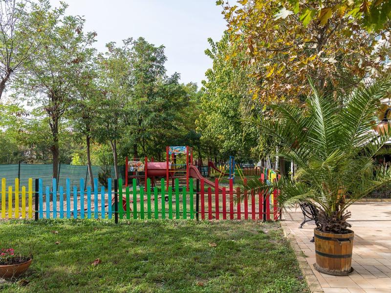 Kleurrijk kinder speelterrein met glijbaan, omgeven door bomen en een geplaveid pad.