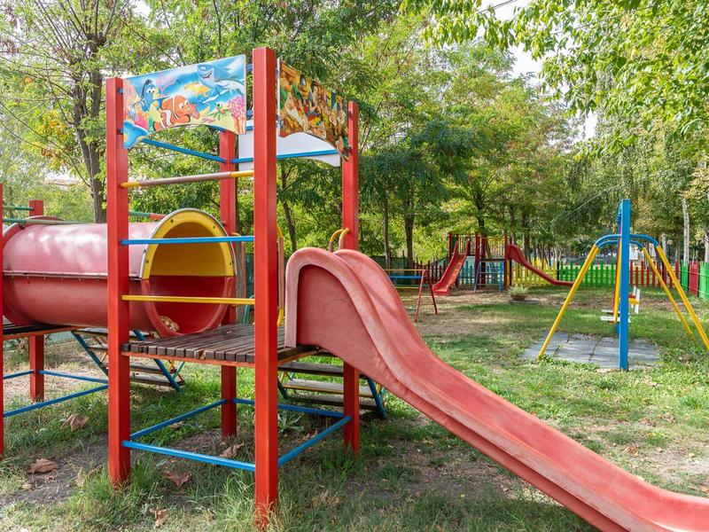 Kleurrijke speeltuin met glijbaan en klimrek buiten onder bomen.