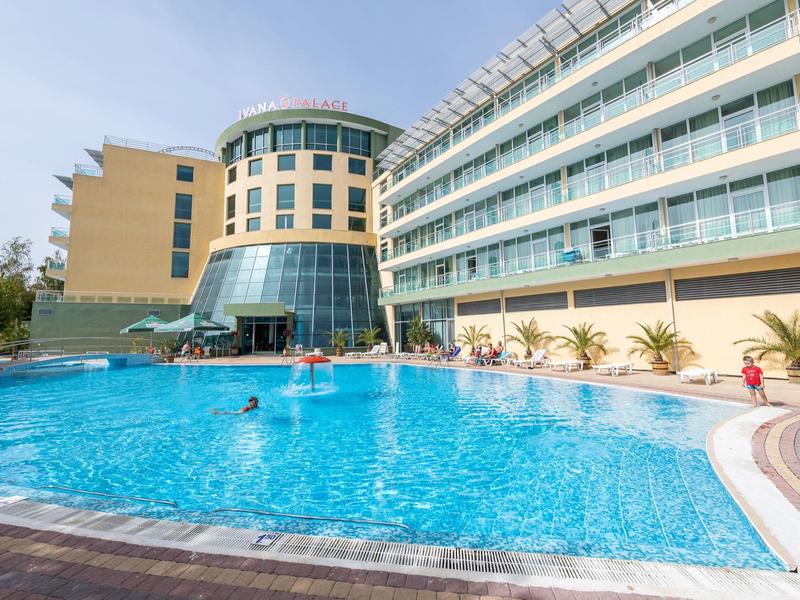 Modern hotel met groot buitenzwembad en parasols onder een heldere hemel.