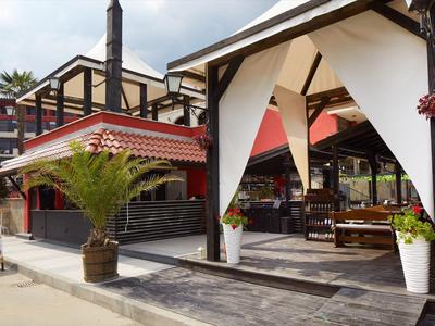 Moderner Außenbereich eines Restaurants mit Holzmöbeln, weißen Vorhängen und Pflanzen in Töpfen.