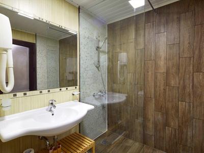 Kleines Badezimmer mit weißem Waschbecken, Spiegel, Holzwandfliesen und Glasdusche.