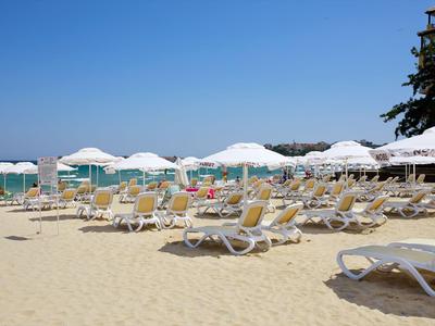 Reihen von Liegestühlen und weißen Sonnenschirmen am Sandstrand mit klarem blauem Himmel.