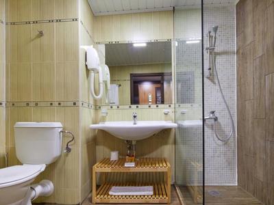 Badezimmer mit weißem WC, Waschbecken, großem Spiegel und Glaskabine mit Dusche, beige Fliesen.