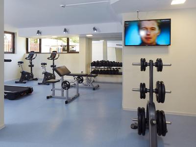 Moderner Fitnessraum mit verschiedenen Trainingsgeräten und Fernseher an der Wand.