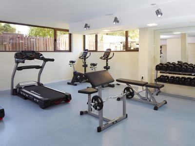 Heller Fitnessraum mit Laufband, Fahrradergometer, Hanteln und Trainingsbank.