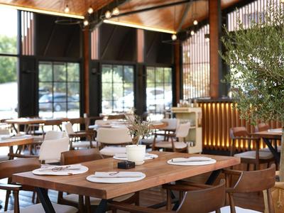 Modernes Restaurant mit Holztischen, braunen Stühlen und großem Fenster im Hintergrund.