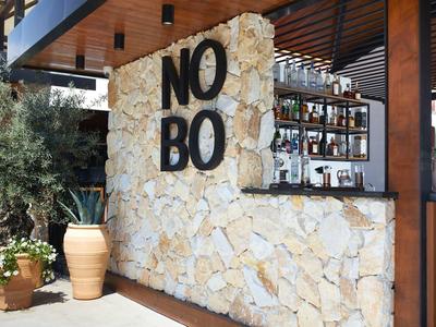 Moderner Außenbarbereich mit Natursteinmauer, großen schwarzen Buchstaben "NO BO" und Pflanzen.