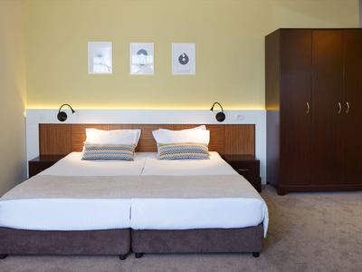 Modernes Schlafzimmer mit Doppelbett, zwei Nachttischlampen, drei Bildern und großem Holzkleiderschrank.