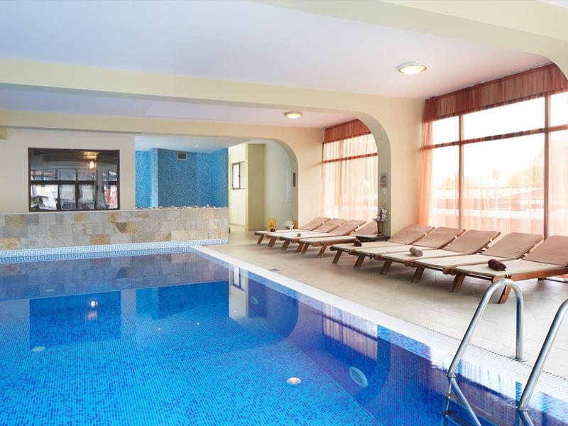 Innenpool mit blauem Wasser, Liegestühlen und großen Fenstern für natürliches Licht.