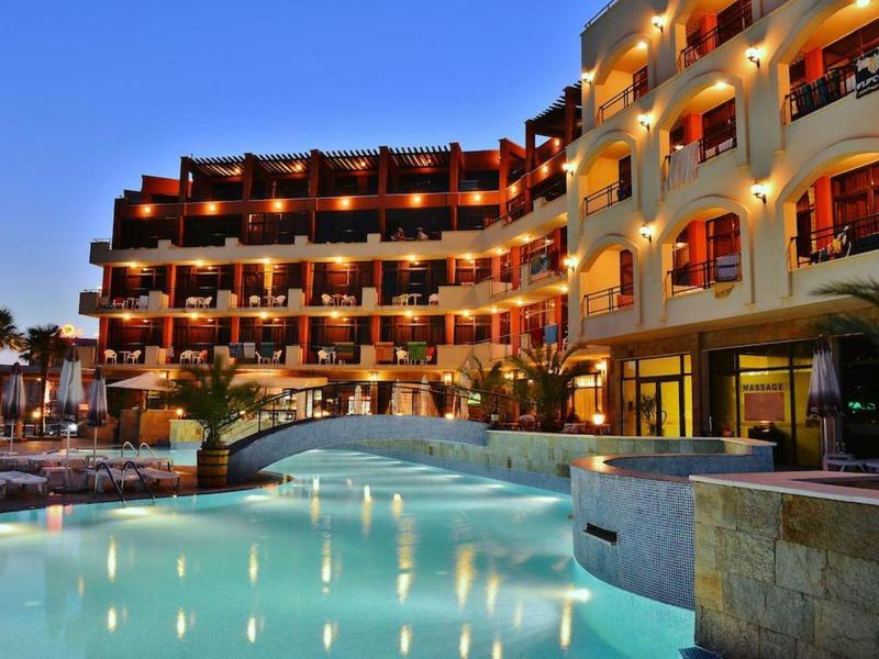 Modernes Hotel mit beleuchtetem Pool und mehreren Stockwerken bei Abenddämmerung.