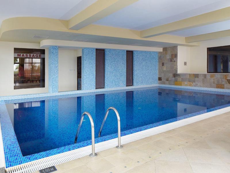 Heller, moderner Innenpool mit blauen Kacheln, Edelstahlleiter und gemütlichen Liegestühlen.