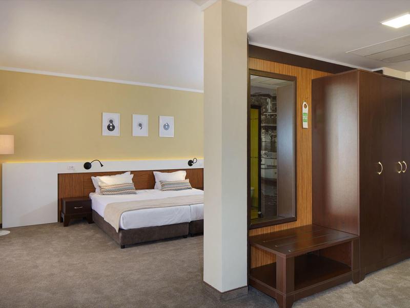 Schlafzimmer mit Doppelbett, Nachttisch, Wandlampen, Kleiderschrank und Sitzbank in warmen Farben.