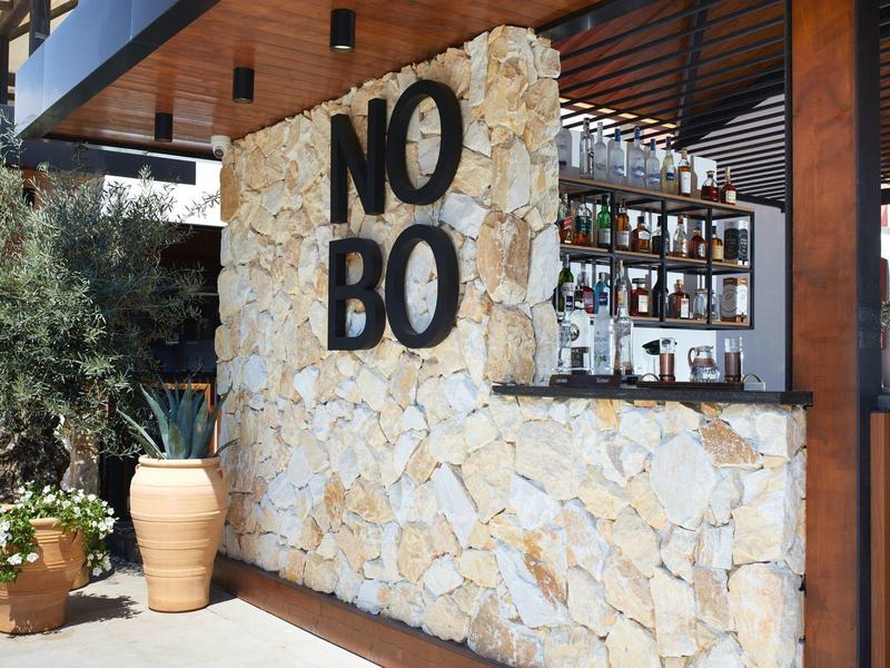 Moderner Außenbarbereich mit Natursteinmauer, großen schwarzen Buchstaben "NO BO" und Pflanzen.
