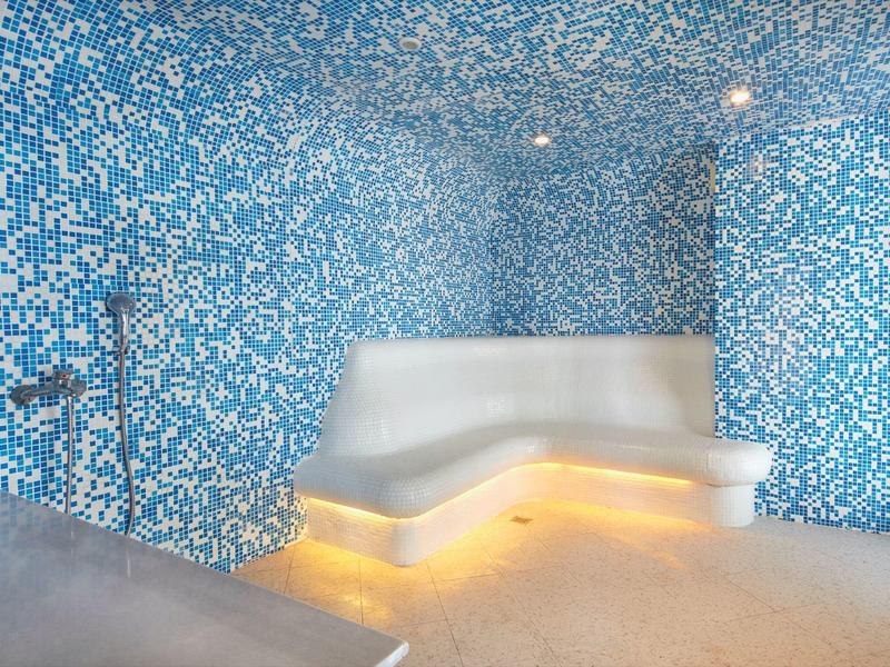 Moderner Raum mit blauen Mosaikfliesen, weißer Bank und warmem indirektem Licht darunter.