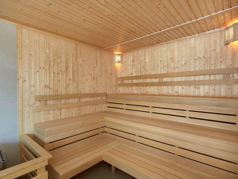 Holzsauna mit L-förmigen Sitzbänken und warmem Licht an den Wänden.