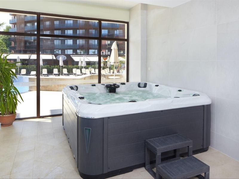 Moderner Whirlpool in hellem Raum mit großen Glasfenstern und Pflanze im Topf daneben.