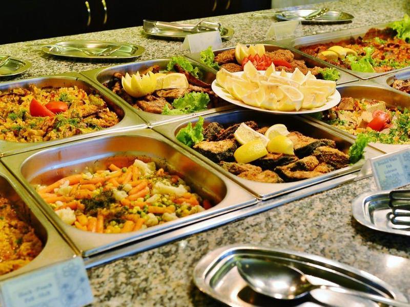 Buffet mit verschiedenen warmen Gerichten in großen Metallbehältern auf Marmorplatte.