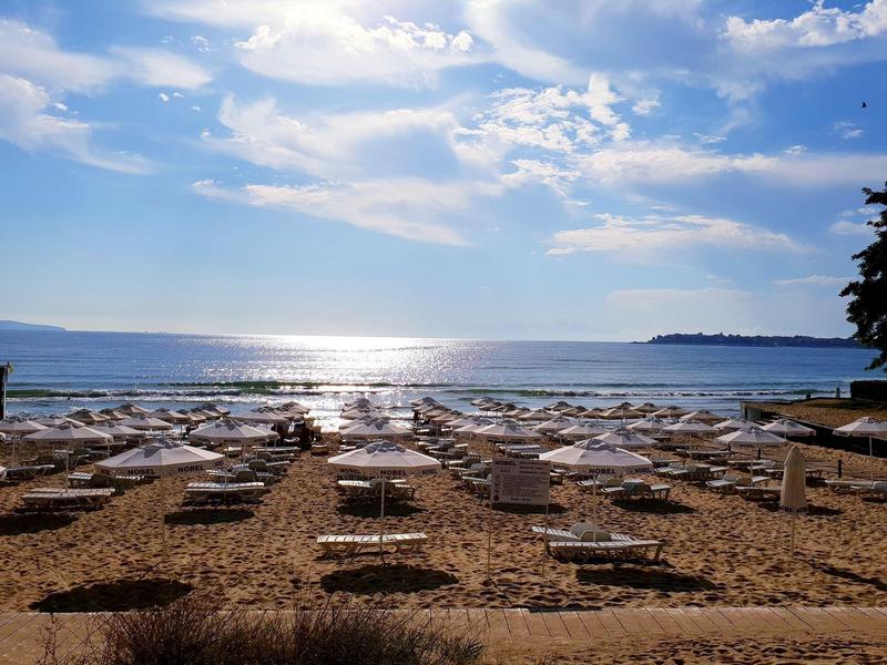 Strand mit vielen leeren Liegen und Sonnenschirmen, Meer und bewölkter Himmel im Hintergrund.