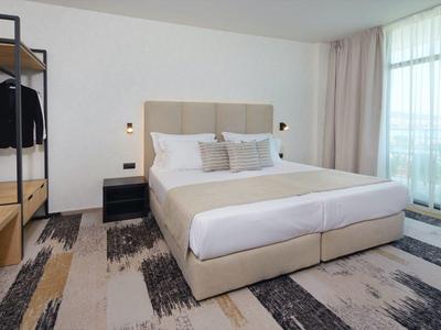 Habitación de hotel moderna con cama grande, alfombra y ventanas de piso a techo con cortinas.
