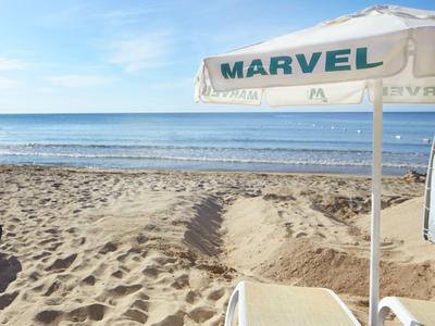 Sandstrand mit Meereshorizont und Sonnenschirm neben Liegestuhl unter blauem Himmel.