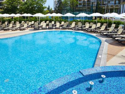 Großer Außenpool mit eingelassener Whirlpool-Ecke und Reihen von Liegestühlen mit weißen Sonnenschirmen.