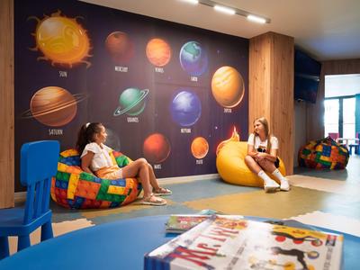 Dos mujeres están sentadas en una habitación colorida con decoración de planetas en la pared, relajándose en pufs.