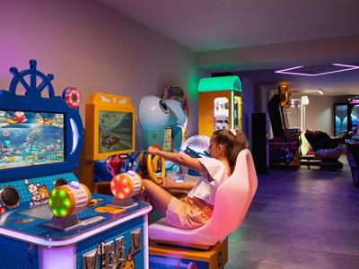 Una joven juega en una sala de juegos colorida con juegos arcade y luz tenue.