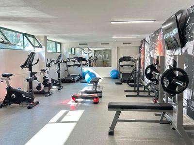 Heller Fitnessraum mit verschiedenen Trainingsgeräten und Hantelbänken.