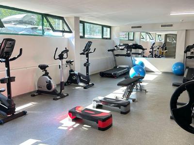 Moderner Fitnessraum mit Cardio-Geräten, Hantelbänken und Spiegeln in hellem Raum.