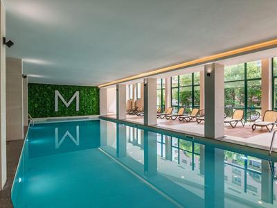 Piscina cubierta con tumbonas y grandes ventanas con vista a árboles verdes