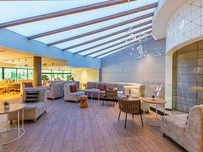 Helle Hotellounge mit modernem Design, Sofas, Sesseln und großen Fenstern unter einem Glasdach.