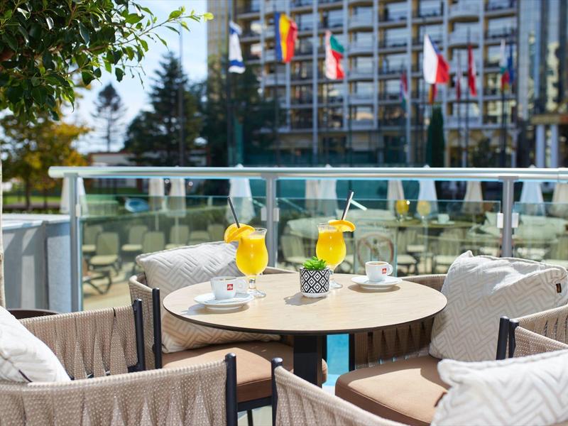 Área de terraza de hotel con mesa, sillas y bebidas en clima soleado
