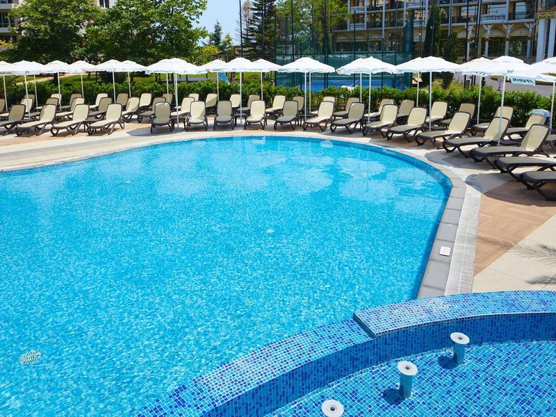 Piscina azul clara de hotel con muchas tumbonas y sombrillas blancas al aire libre.