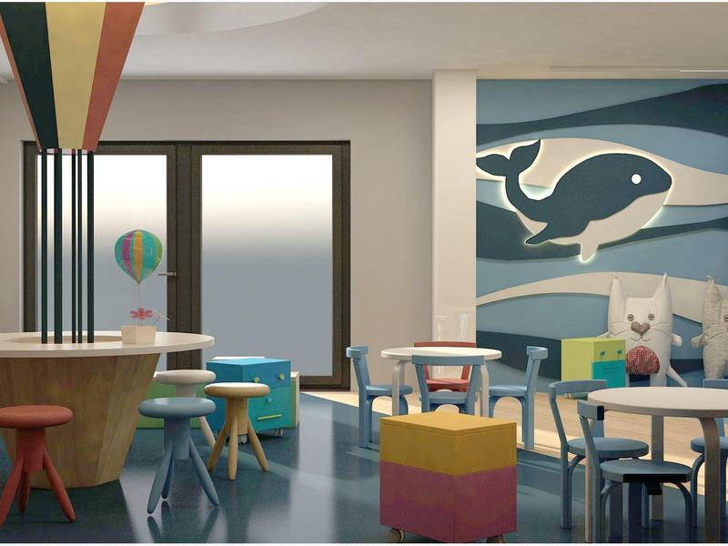 Zona infantil luminosa y colorida con mesas, sillas de colores y un mural de ballena en la pared.